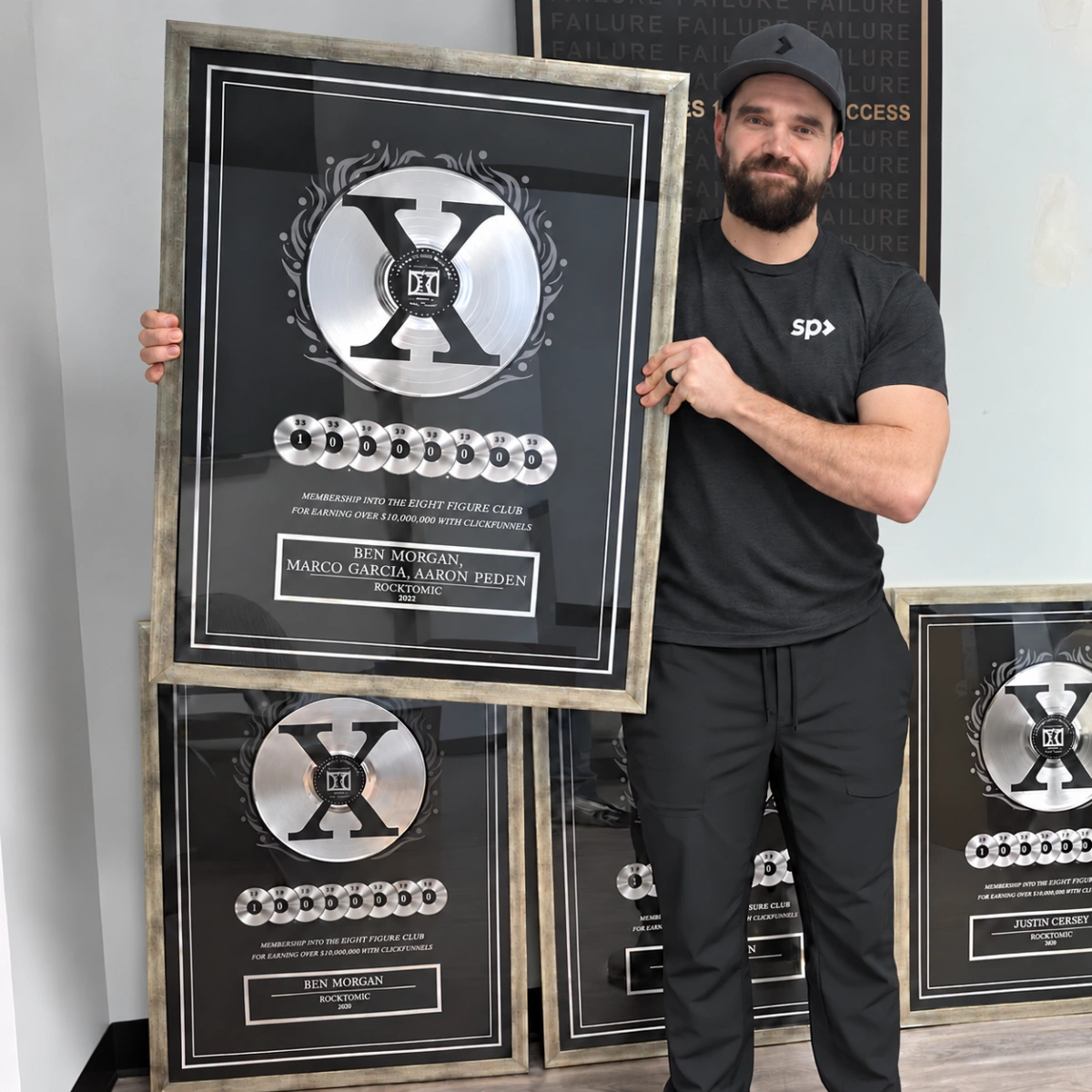 Aaron Peden holding Rocktomic’s team award, surrounded by plaques